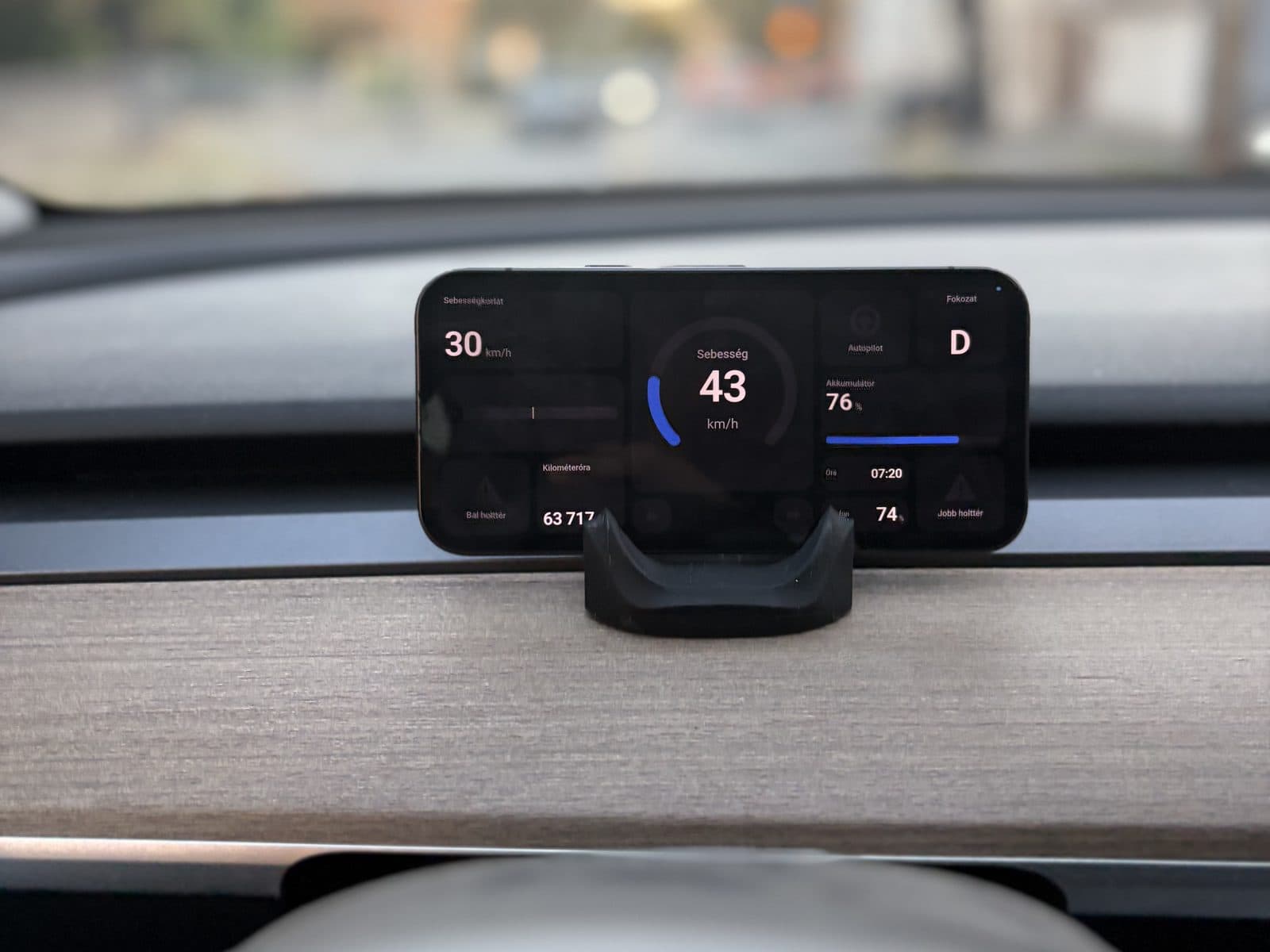 A phone running DashPilot in a stand on a Tesla dashboard, showing speed, gear, battery and the speed limit
